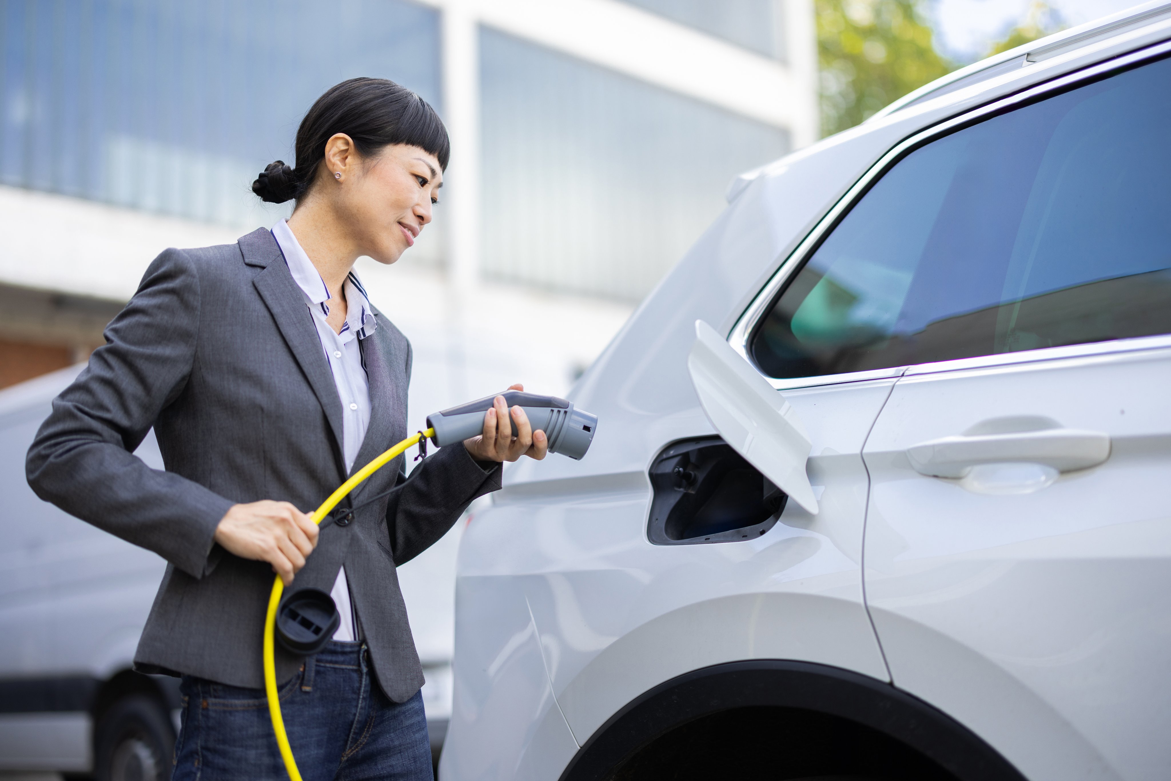 Happy Asian businesswoman charging her electric car at the charging station