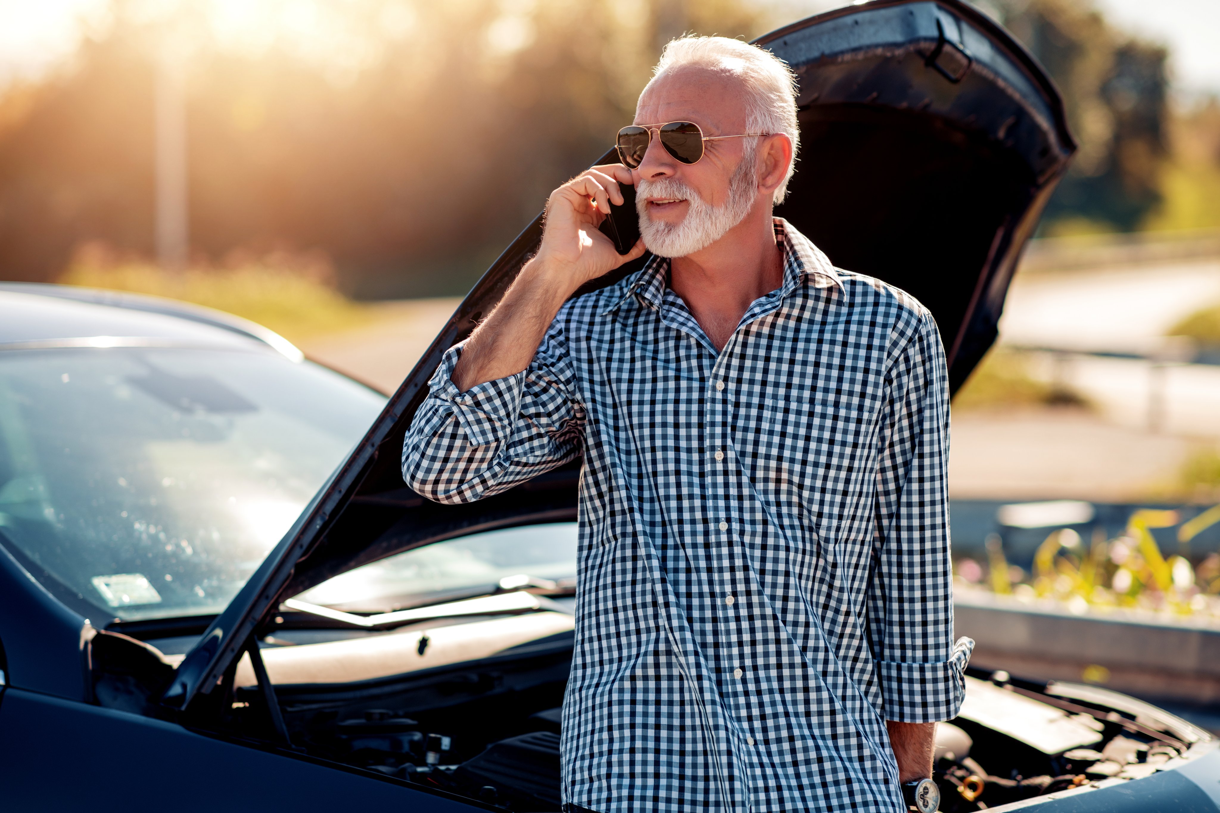 Man on the side of the road leaning against his car with the hood up, calling for automobile help.