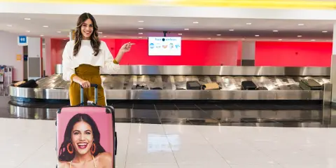 Woman with her travel luggage standing in an airport with the luggage carousel behind her