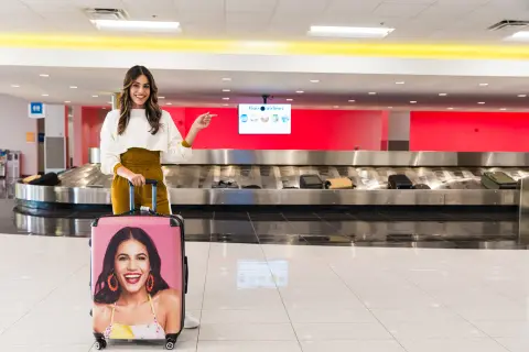 Woman with her travel luggage standing in an airport with the luggage carousel behind her