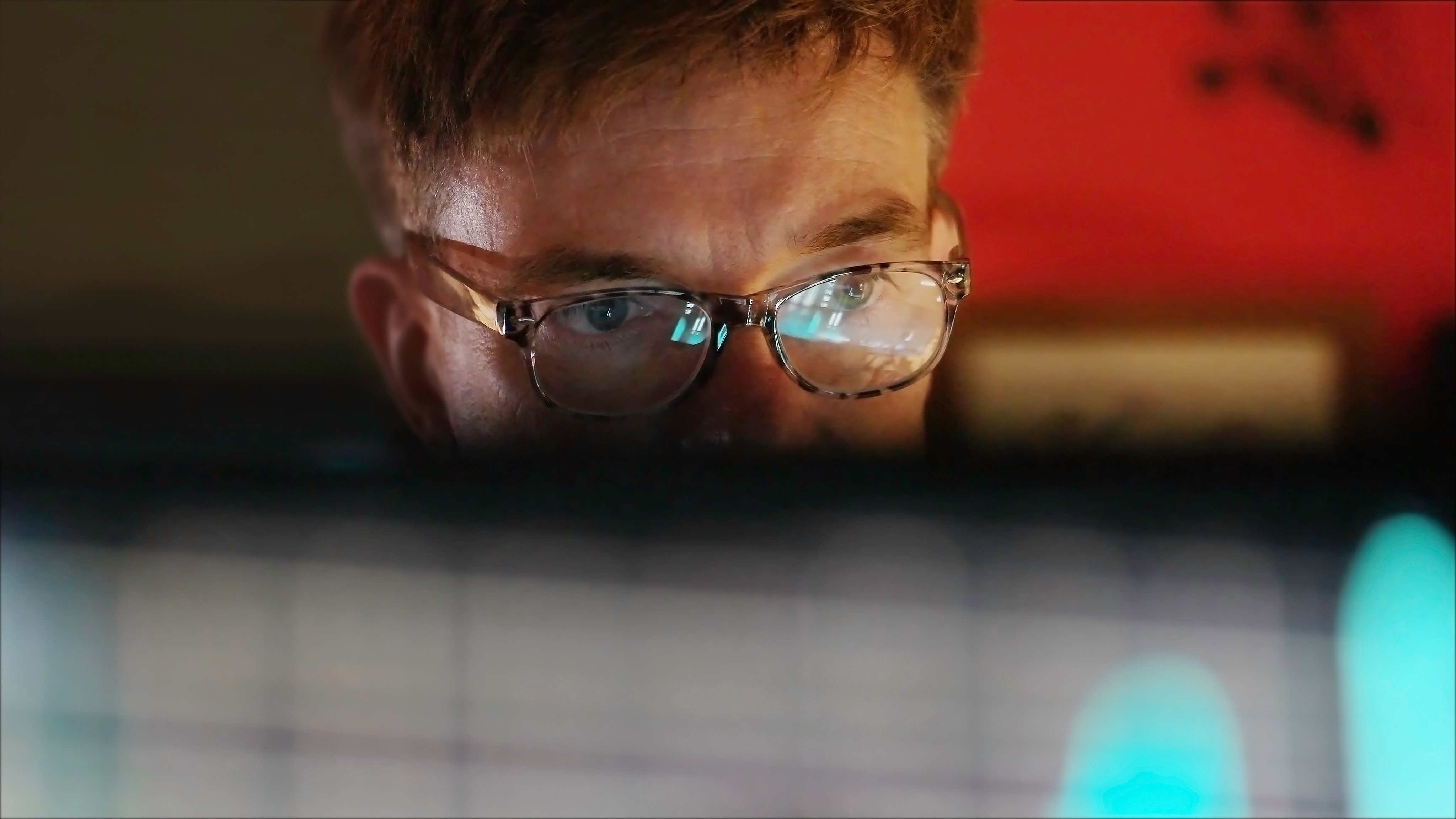 A mature man studying a colourful computer display which is reflected in his glasses.