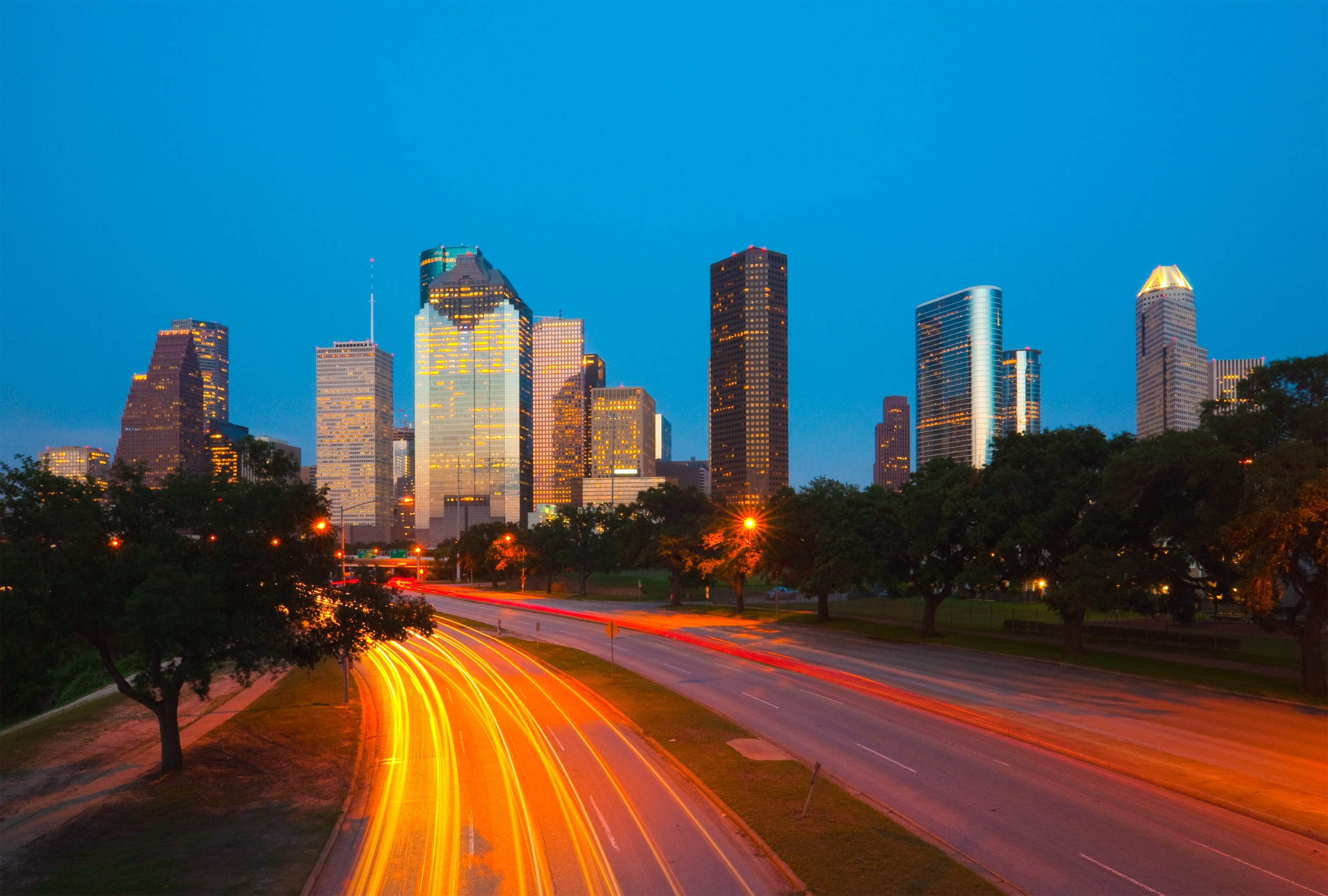 Houston downtown skyline at dusk with light trails on Allen Parkway in the foreground.