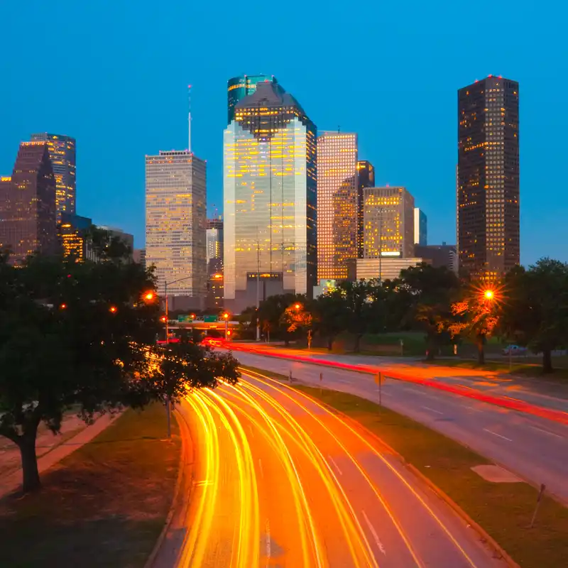 Houston downtown skyline at dusk with light trails on Allen Parkway in the foreground.