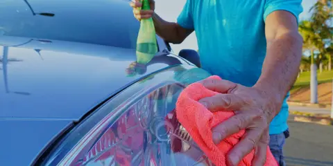 Person cleaning a car headlight with a cloth and spray bottle