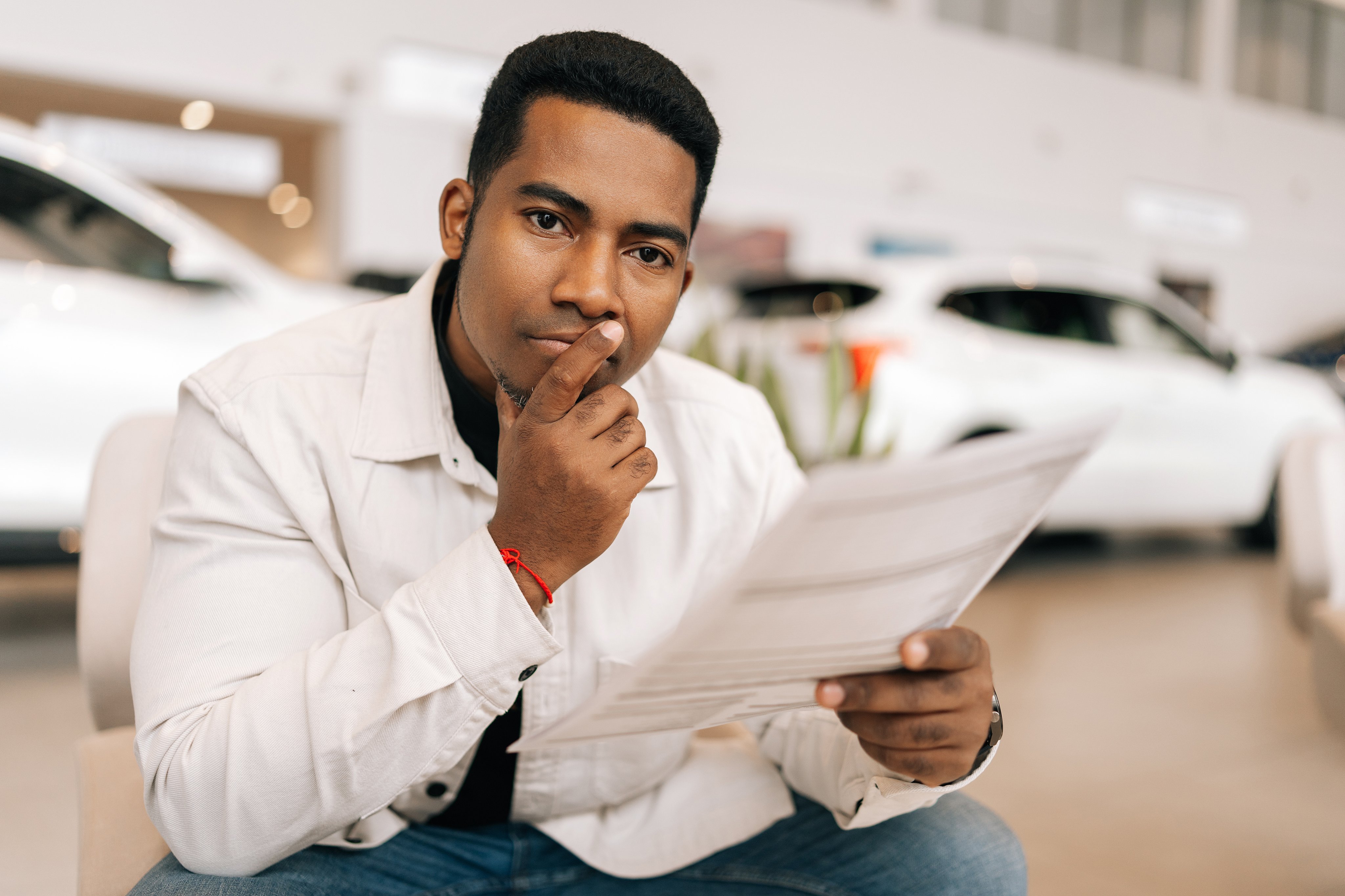 Portrait of doubtful African-American male buyer reading car purchase agreement before signing in dealership office