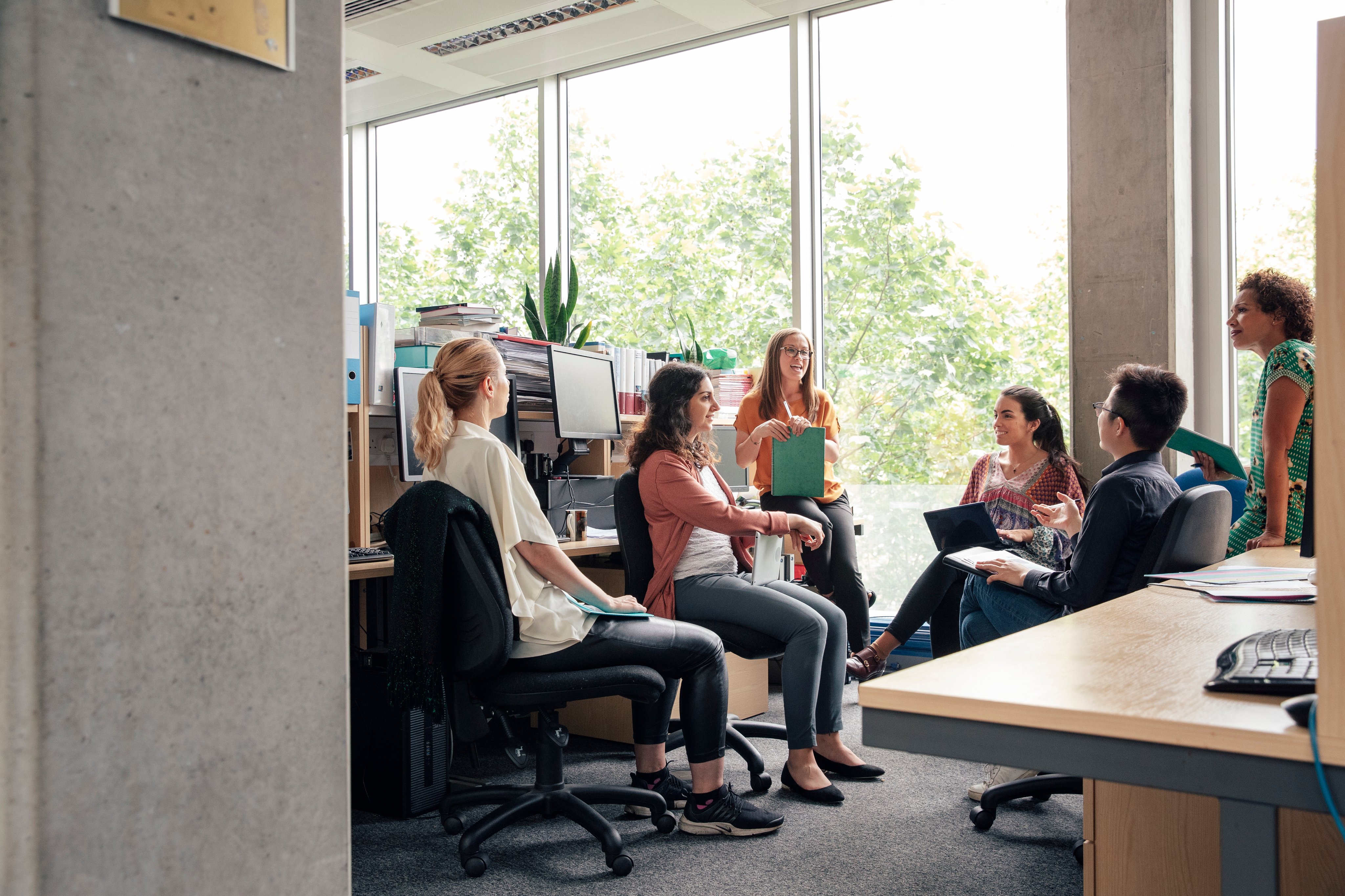 A group of graduates sitting casually around desks, having an informal discussion.