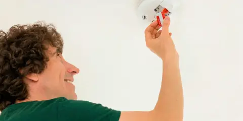 Person installing a new battery in a ceiling-mounted smoke detector