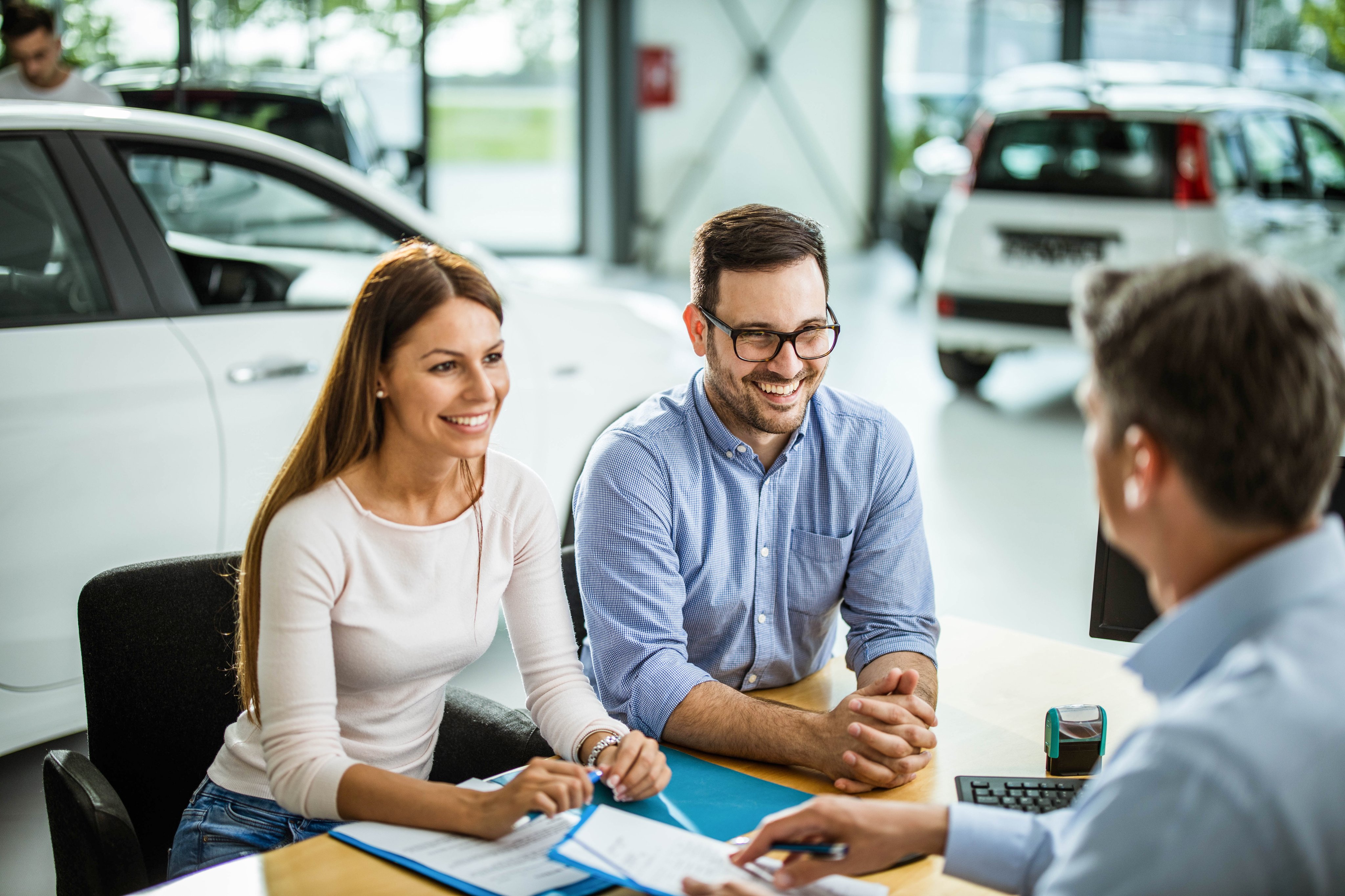 Happy couple shopping and talking to salesperson in a car showroom