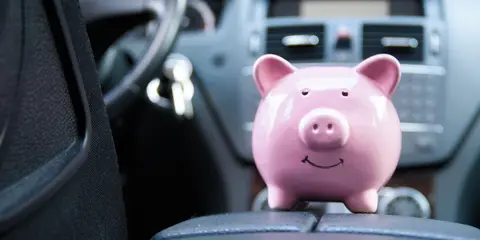 Piggy bank on a car center console representing 'drive less, pay less' auto insurance savings