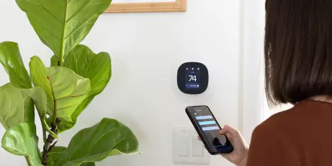 Woman setting up a smart thermostat with smartphone