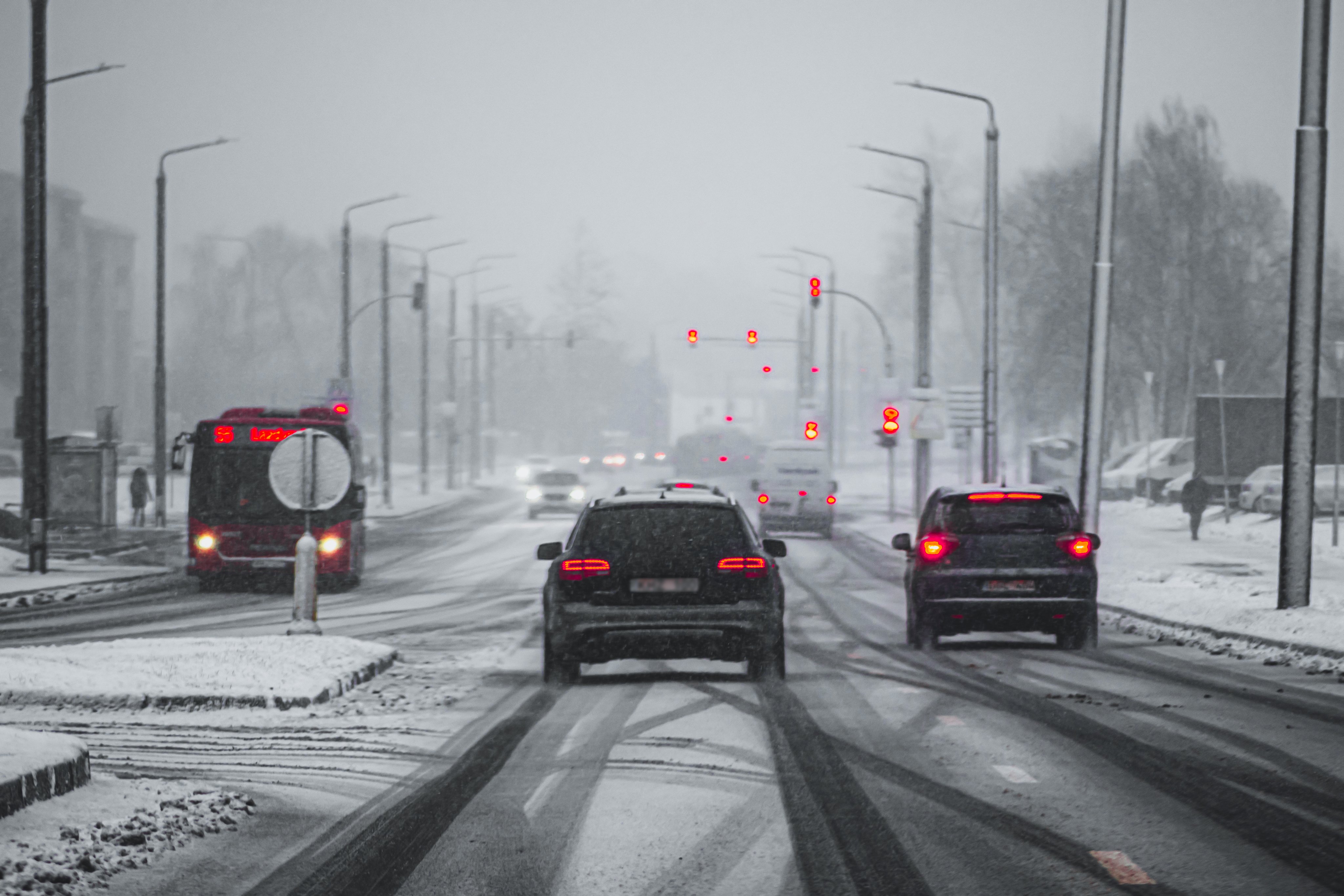 Perspective artistic view of a road during a snow storm, with red lights from cars and traffic lights