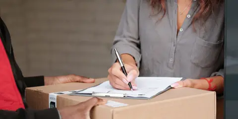 Person signing for a delivered package while a courier hands over the box