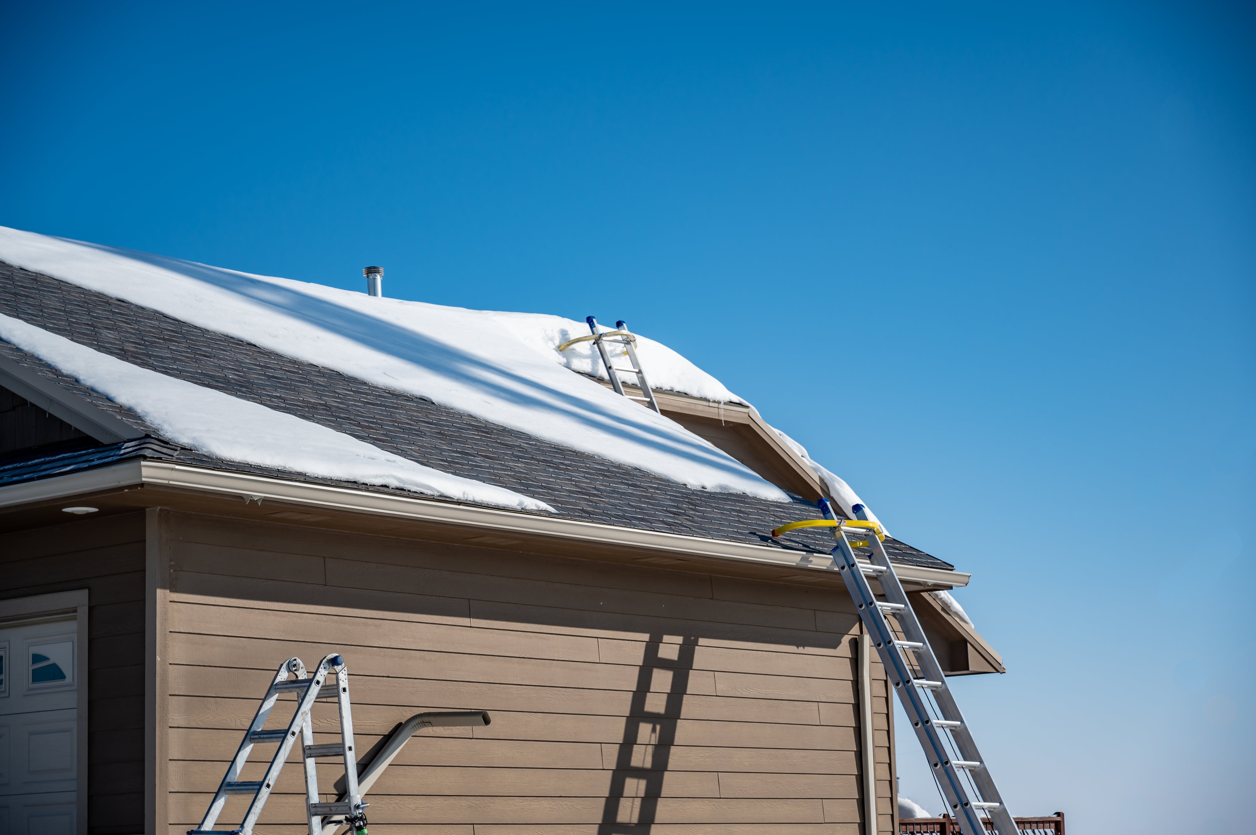 Ladder and safety hook on a residential roof covered in snow as gutters are being installed
