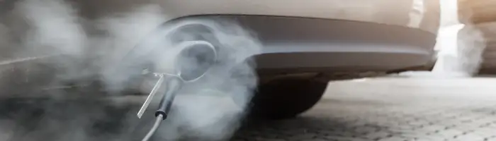 Car exhaust pipe emits dense smoke during emission test on city pavement. Pollution control device measures harmful gases. Service car center garage workshop