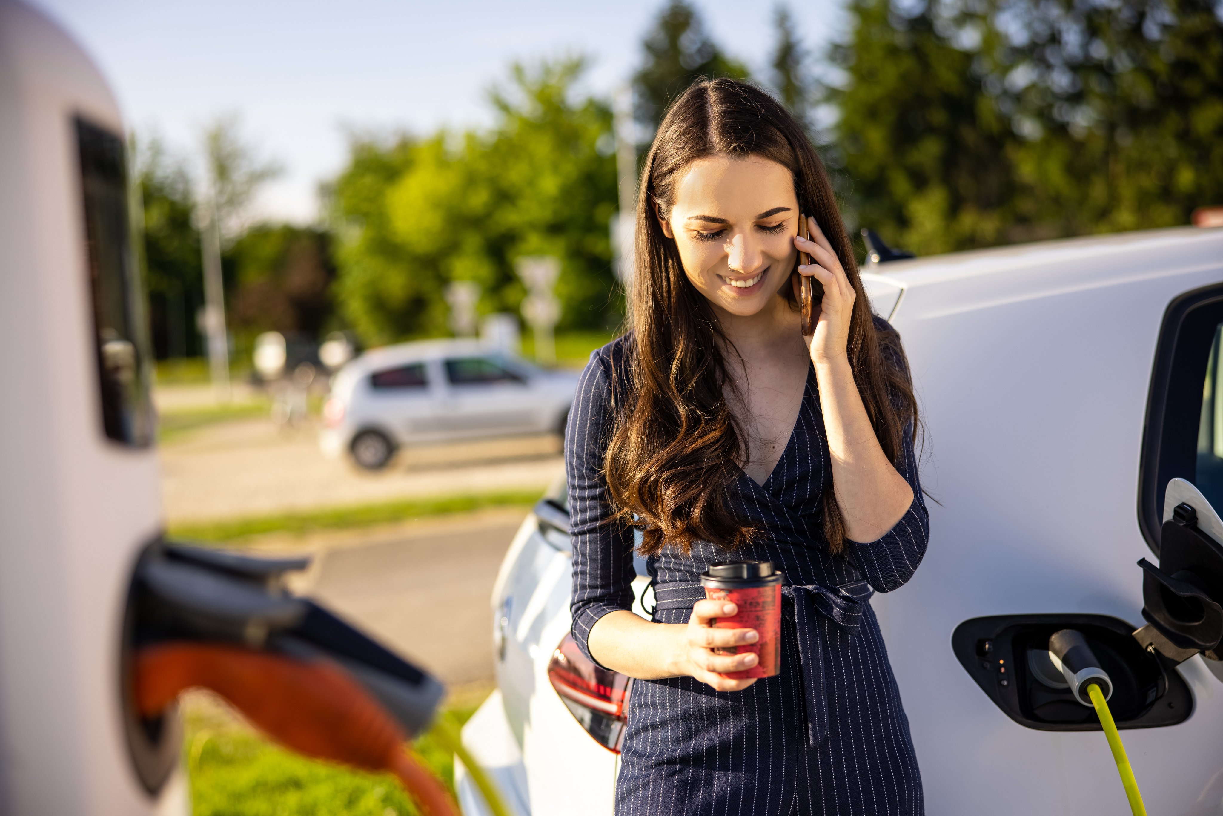 Young woman talking on mobile phone while waiting for electric car to charge