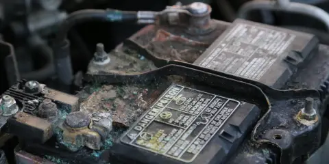 Close-up of a corroded car battery with buildup on the terminals and visible signs of wear and oxidation