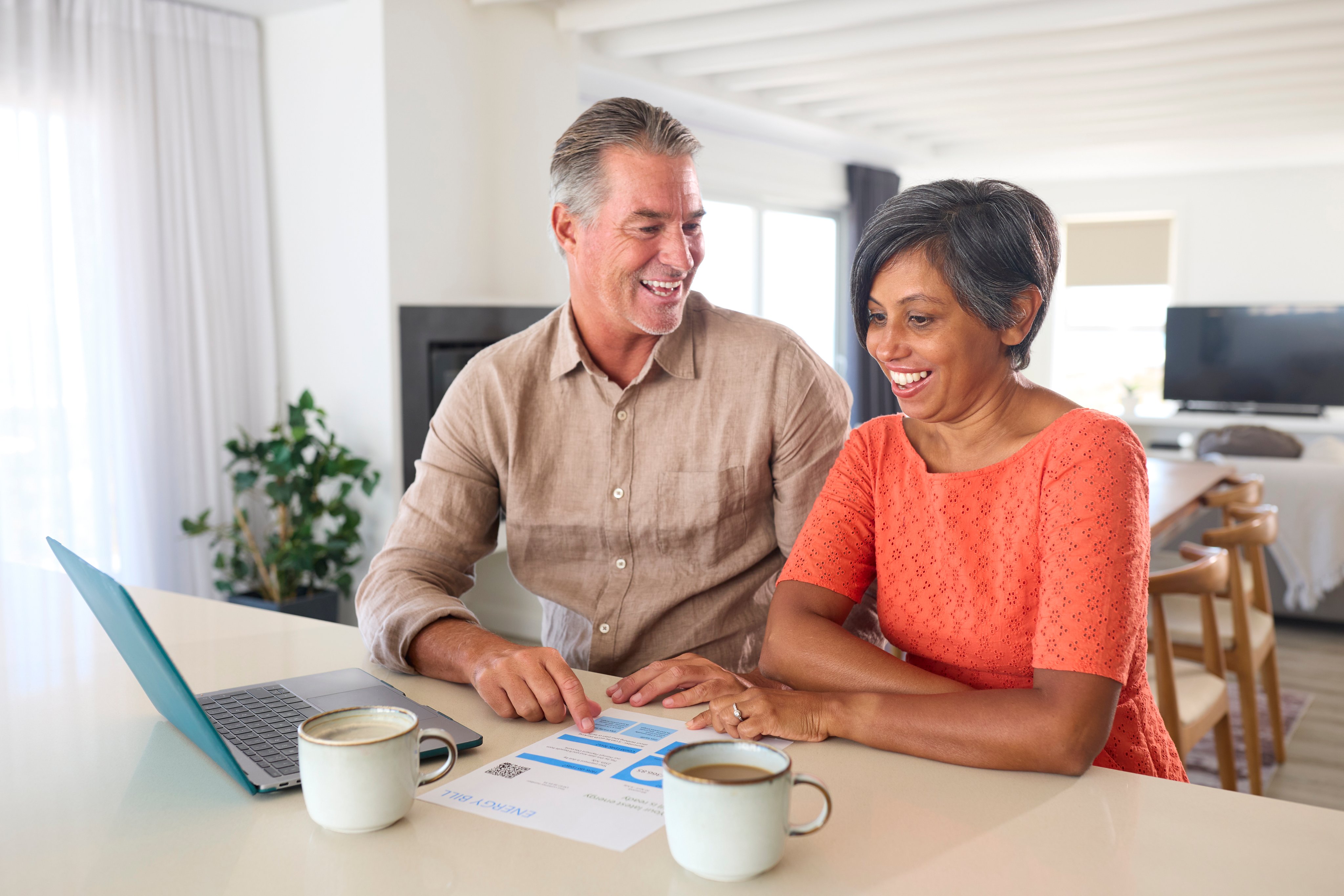 Smiling mature couple at home with laptop looking at bill