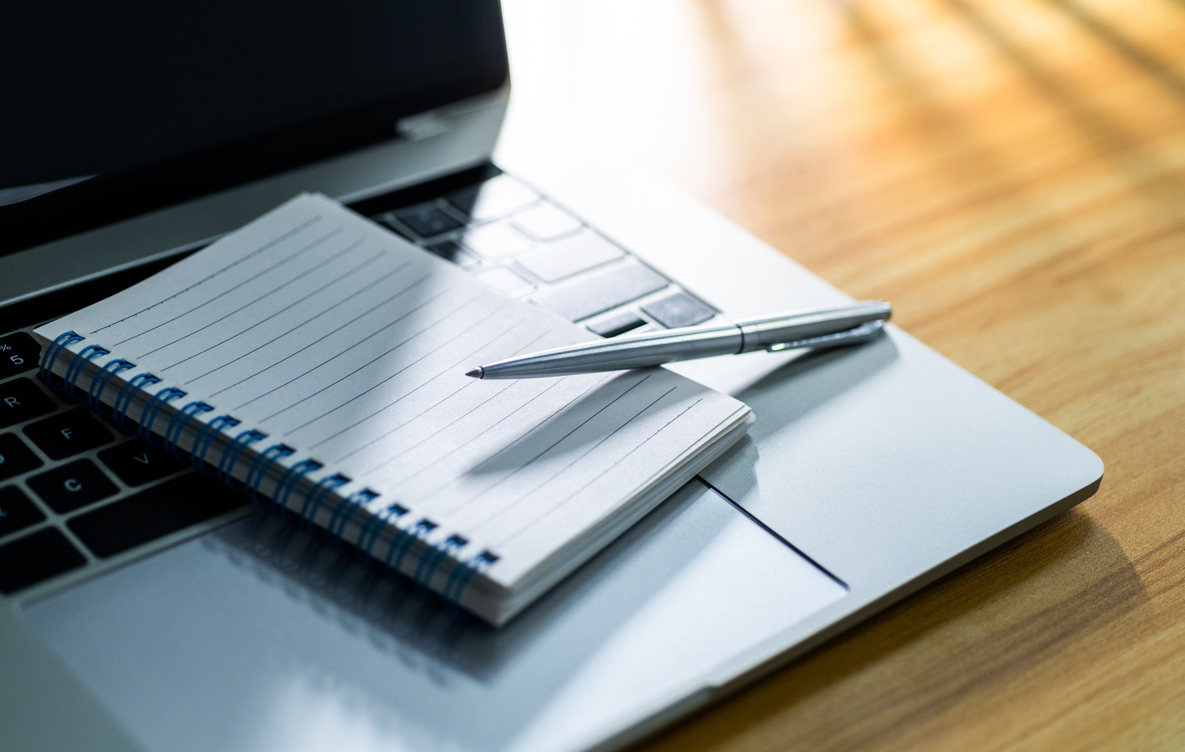 Laptop computer with pen and spiral notebook on desk