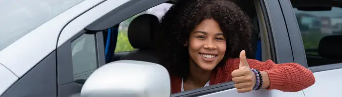 Young woman half asian half African shows thumb up inside of new modern car