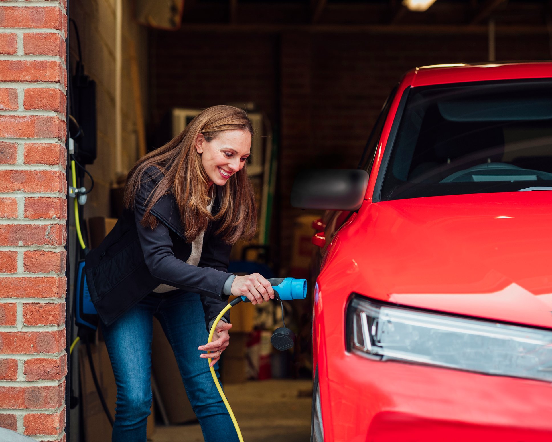 Adult woman plugs her electric car in to charge within garage