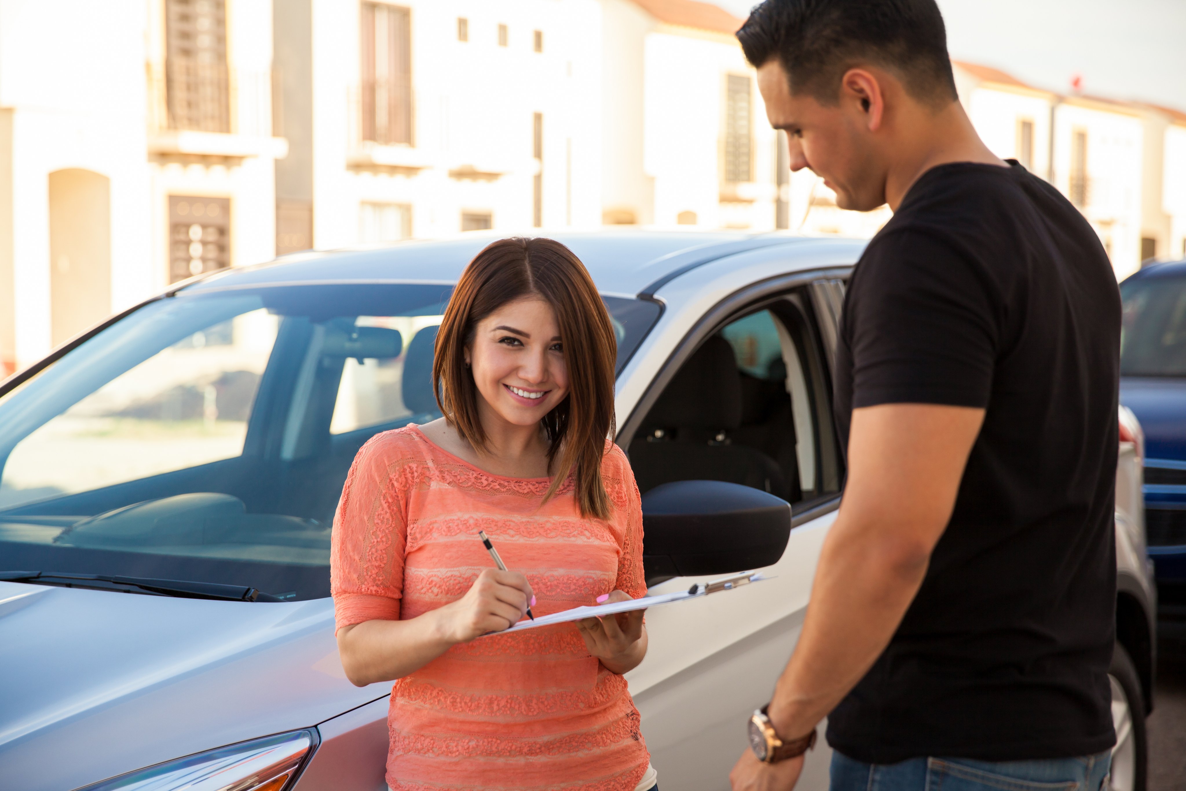 Happy young woman shopping for insurance with an agent beside her car
