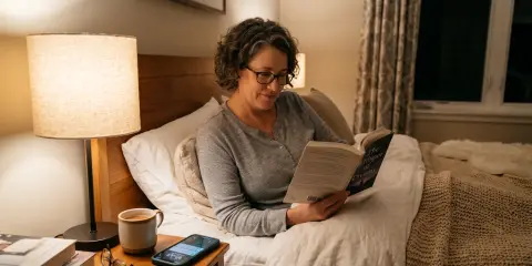 Lady in bed reading a book with her mobile phone on the nightstand