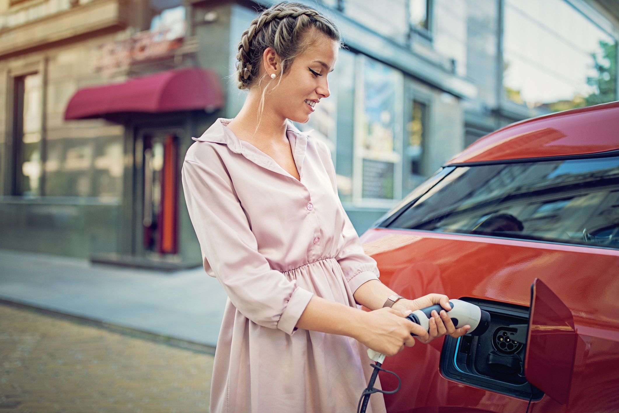 Young woman charging her electric car in the city
