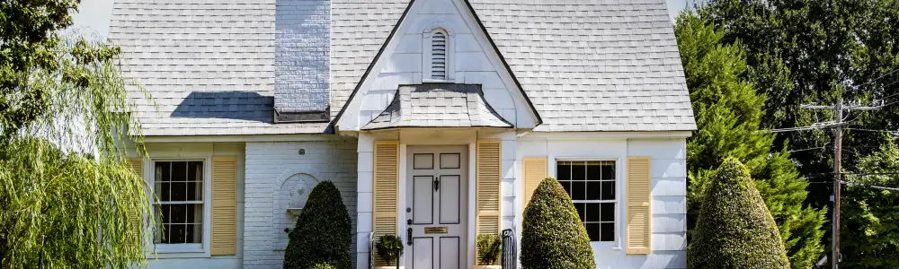 Cute yellow and white brick and siding cottage in Tulsa with pretty lawn and landscaping and shutters in leafy neighborhood
