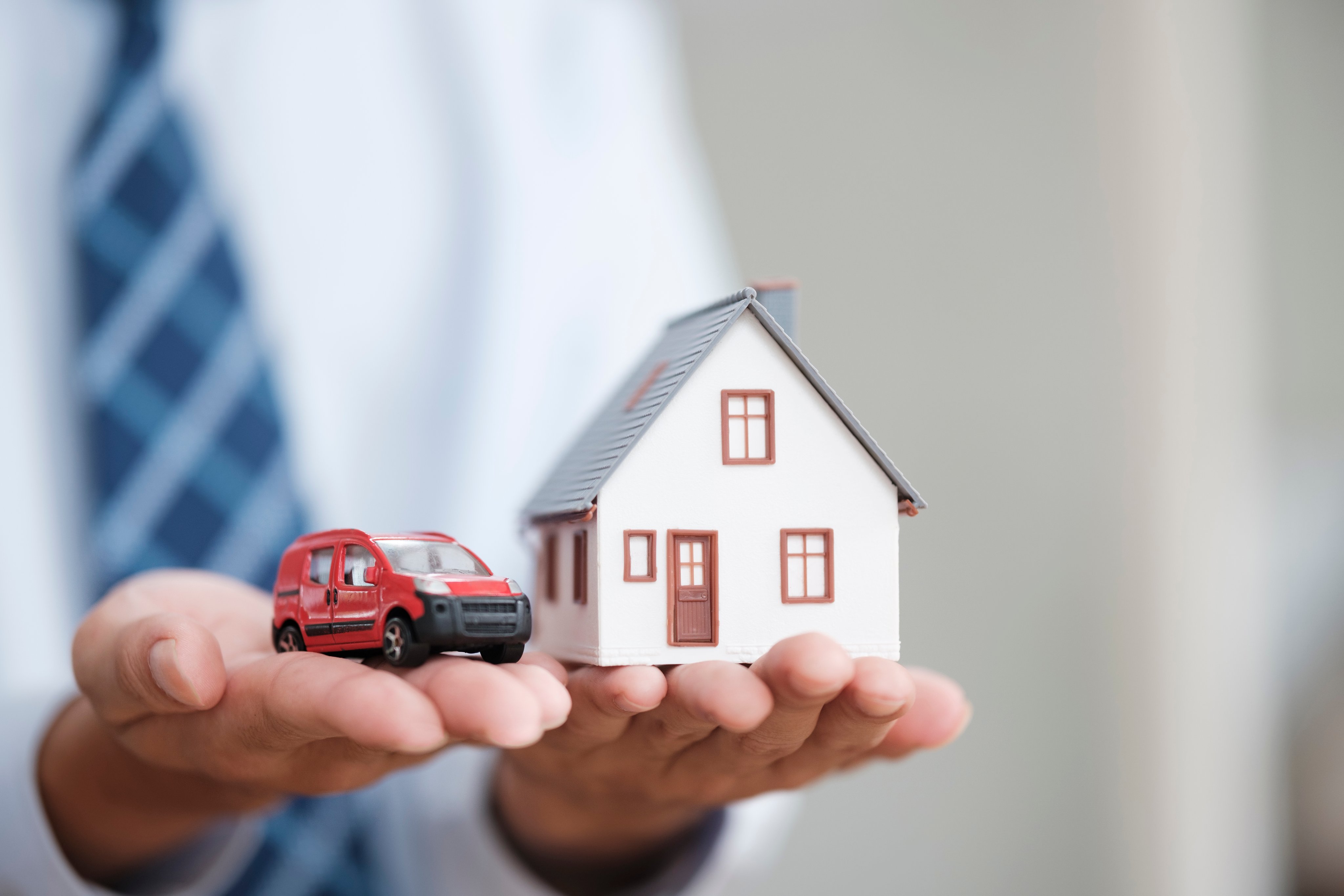 Hands holding a car and a house, symbolizing bundled home and auto insurance.