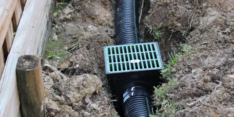 French drain system installed in a narrow trench beside a wooden retaining wall