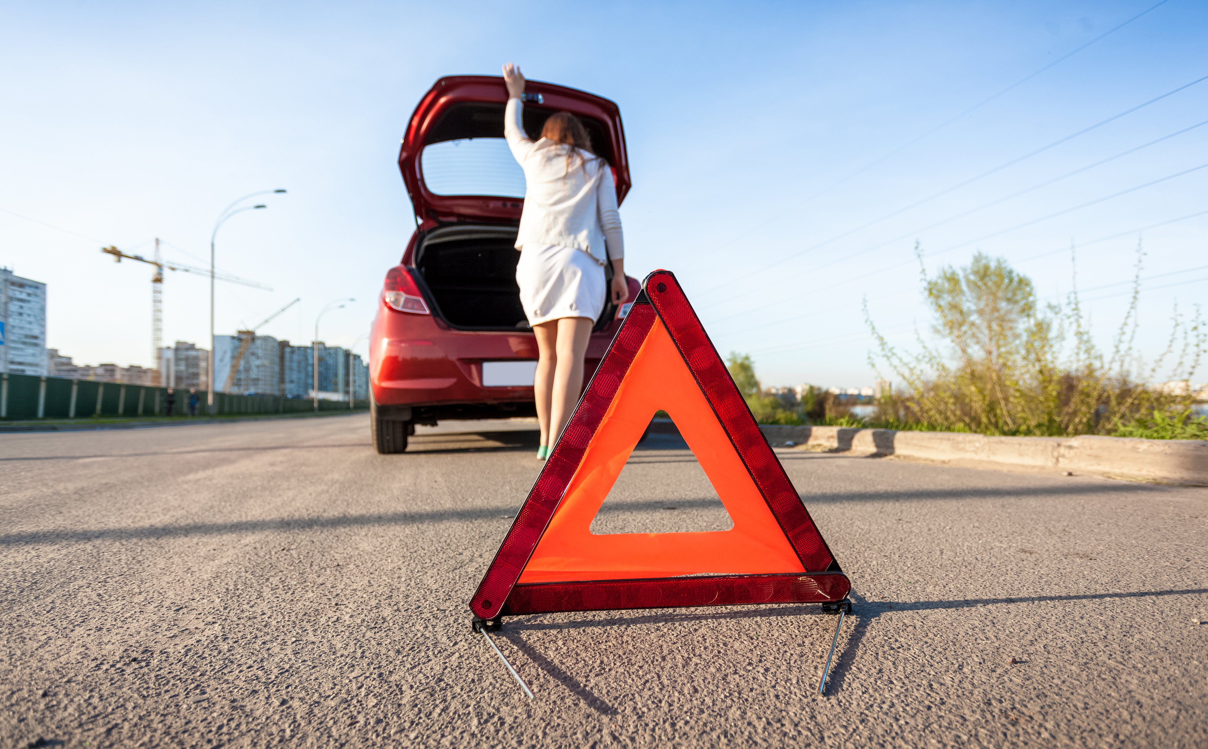 Woman opening trunk and placing hazard sign by car