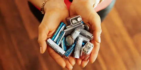Hands holding a pile of used household batteries
