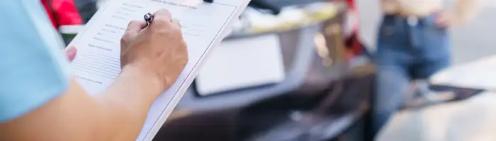 Insurance agent filling out vehicle accident claim form on clipboard