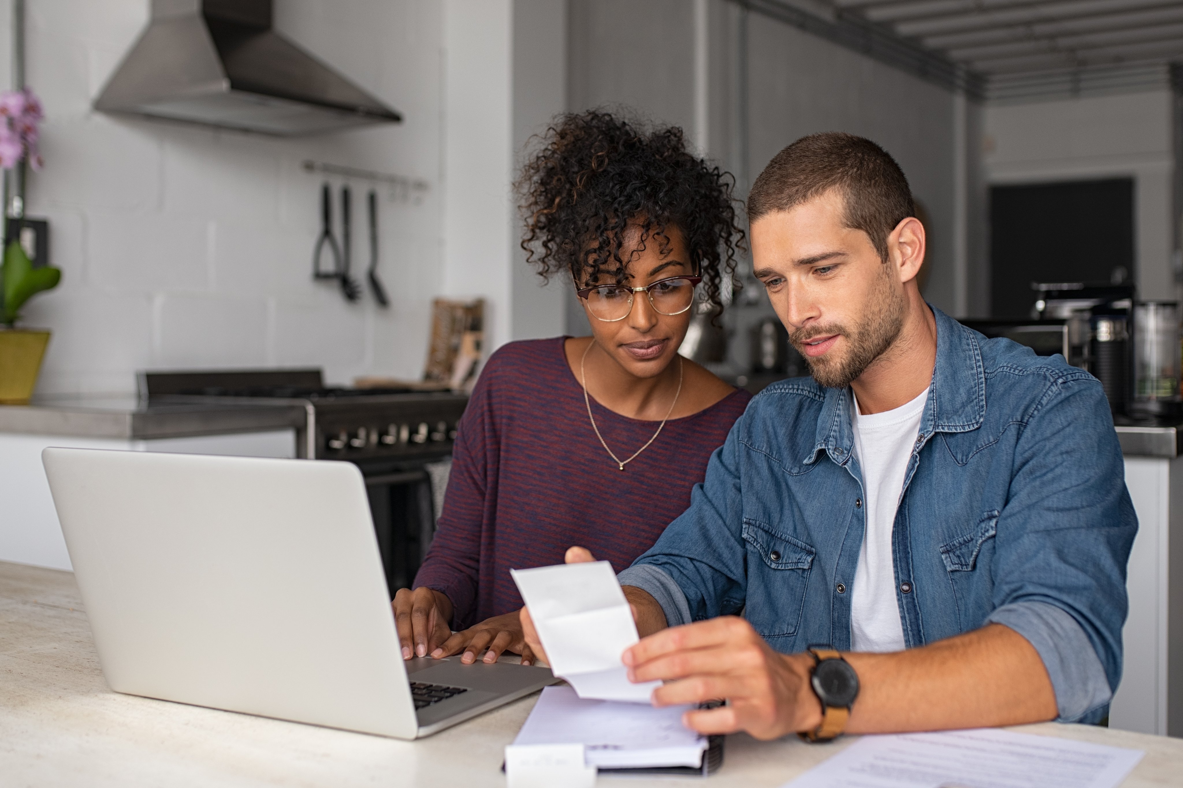 Young multiethnic couple checking bills while managing accounts on home banking app