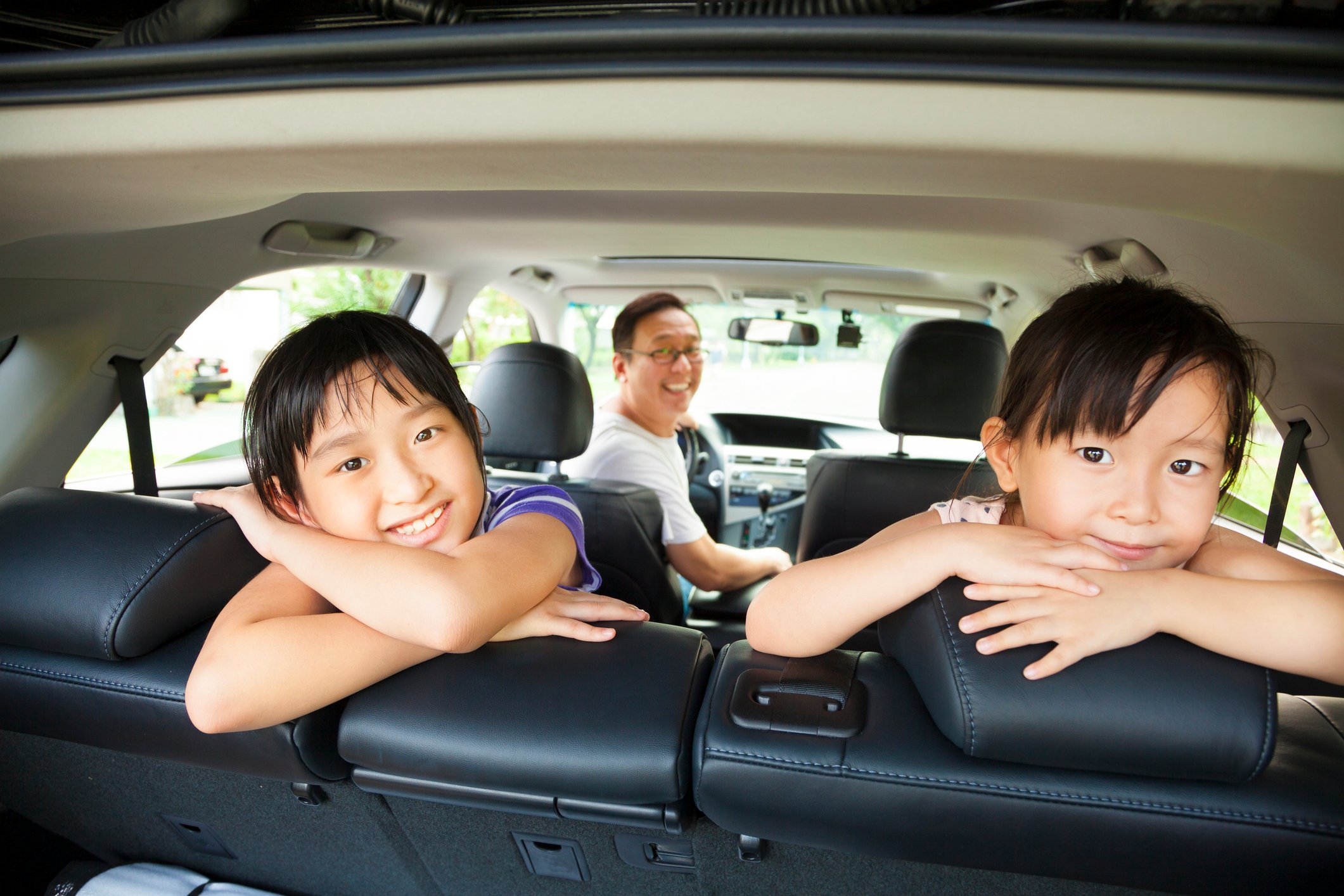 Smiling dad and 2 daughters sitting in new SUV