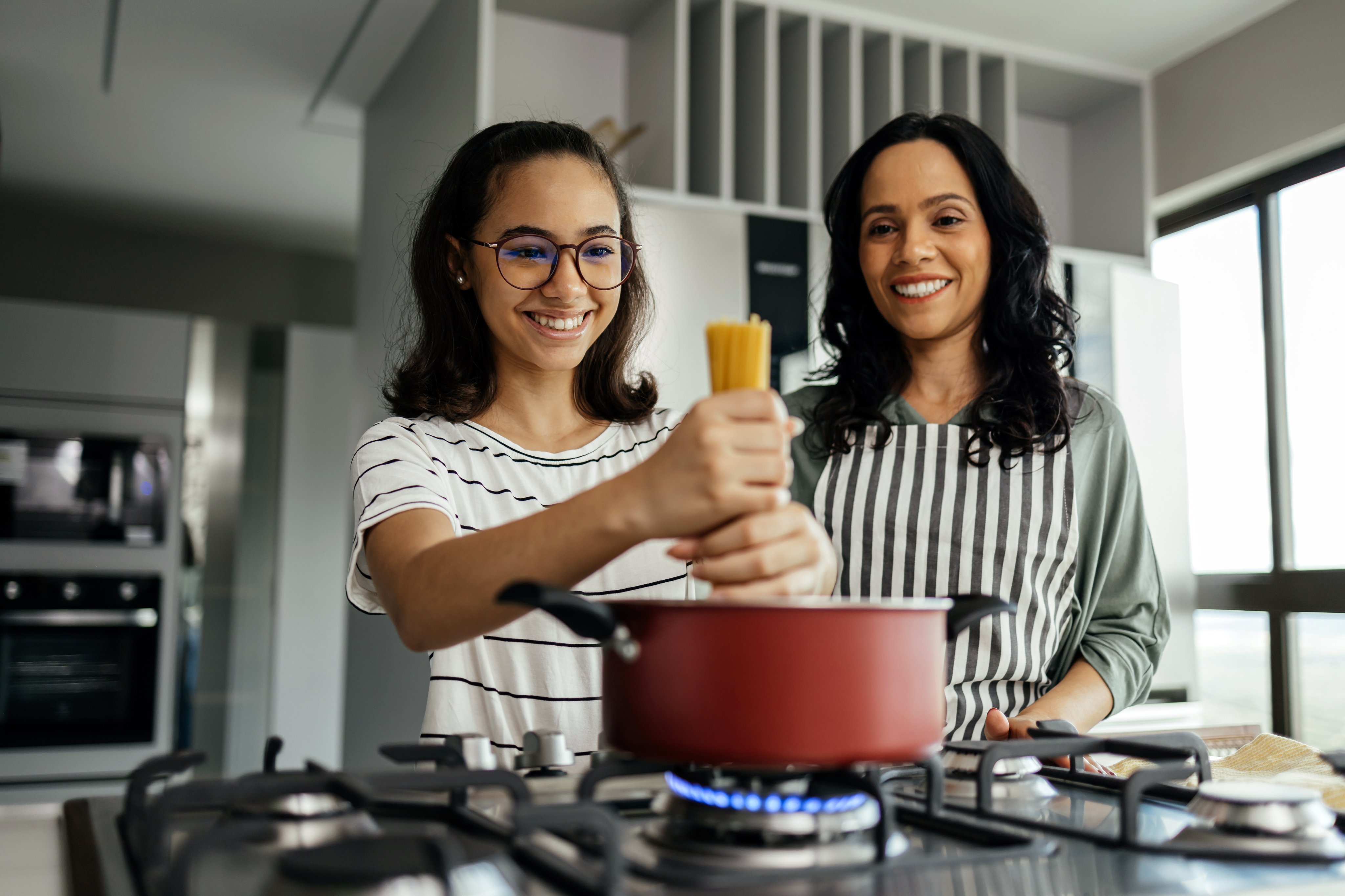 A mother and her teenage daughter joyfully cooking together in the kitchen, sharing laughter and creating a delicious meal.