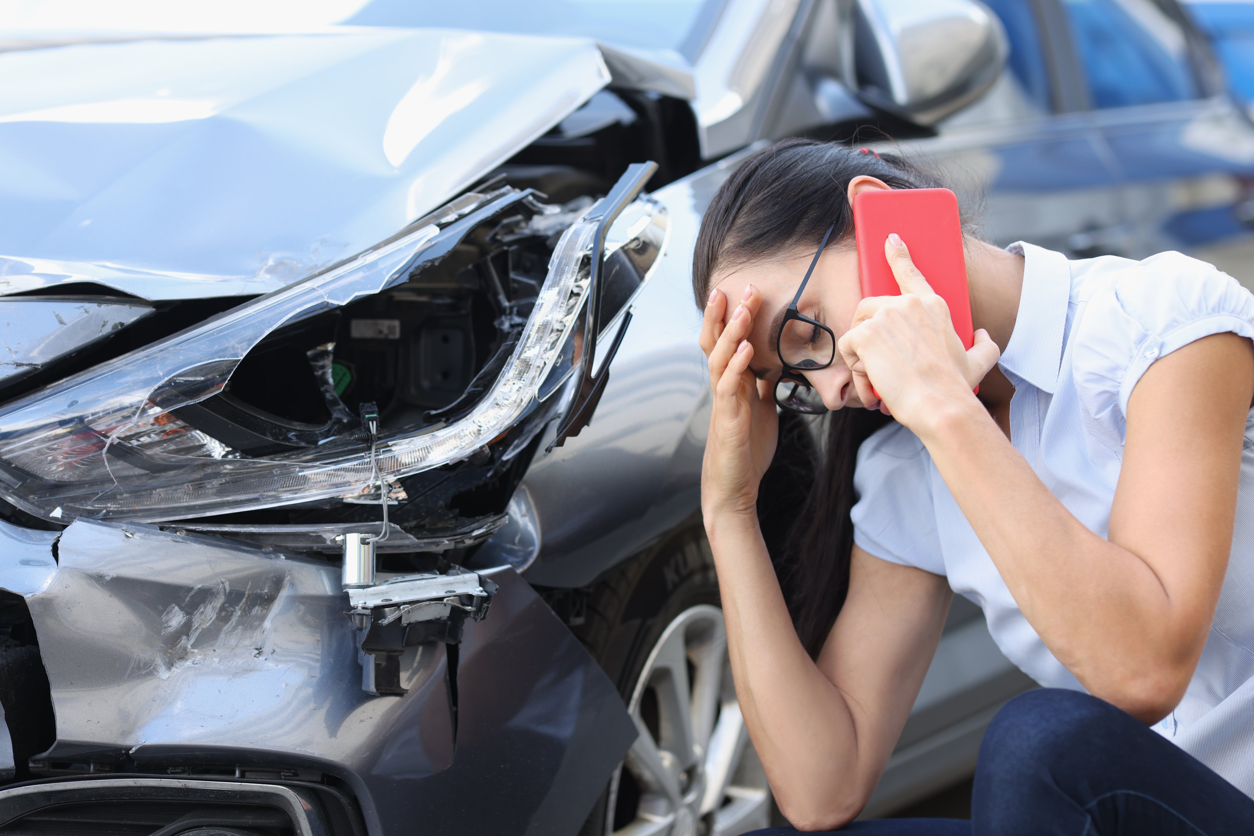 Sad woman talking on cell phone near wrecked car.