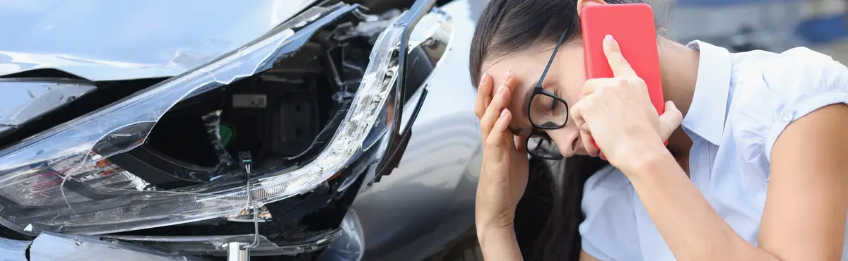 Sad woman talking on cell phone near wrecked car