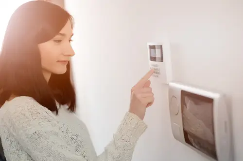 Young brunette woman entering code on keypad of home security alarm. Video intercom next to alarm keypad