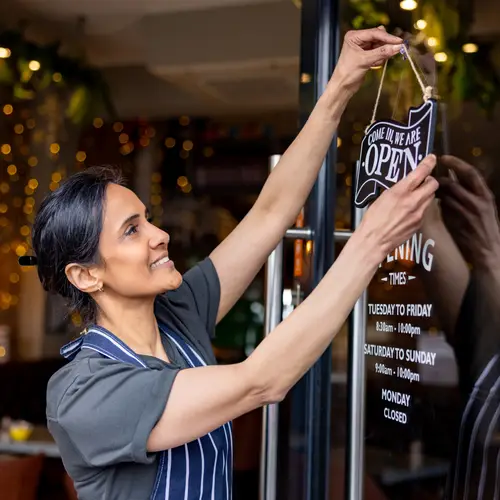 Happy female business owner hanging an open sign on the door at a cafe - small business concepts