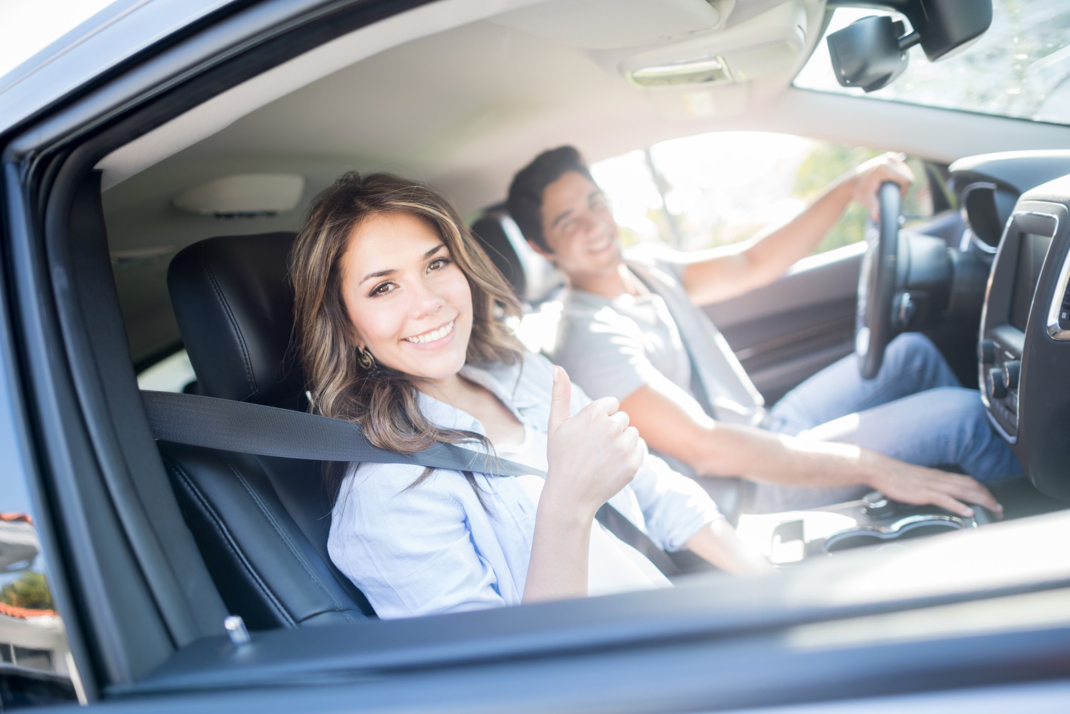 Young happy couple sitting in front seat of car and giving the thumbs up