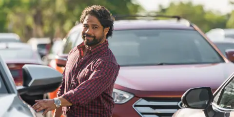 Man standing next to a parked SUV in a shopping center parking lot
