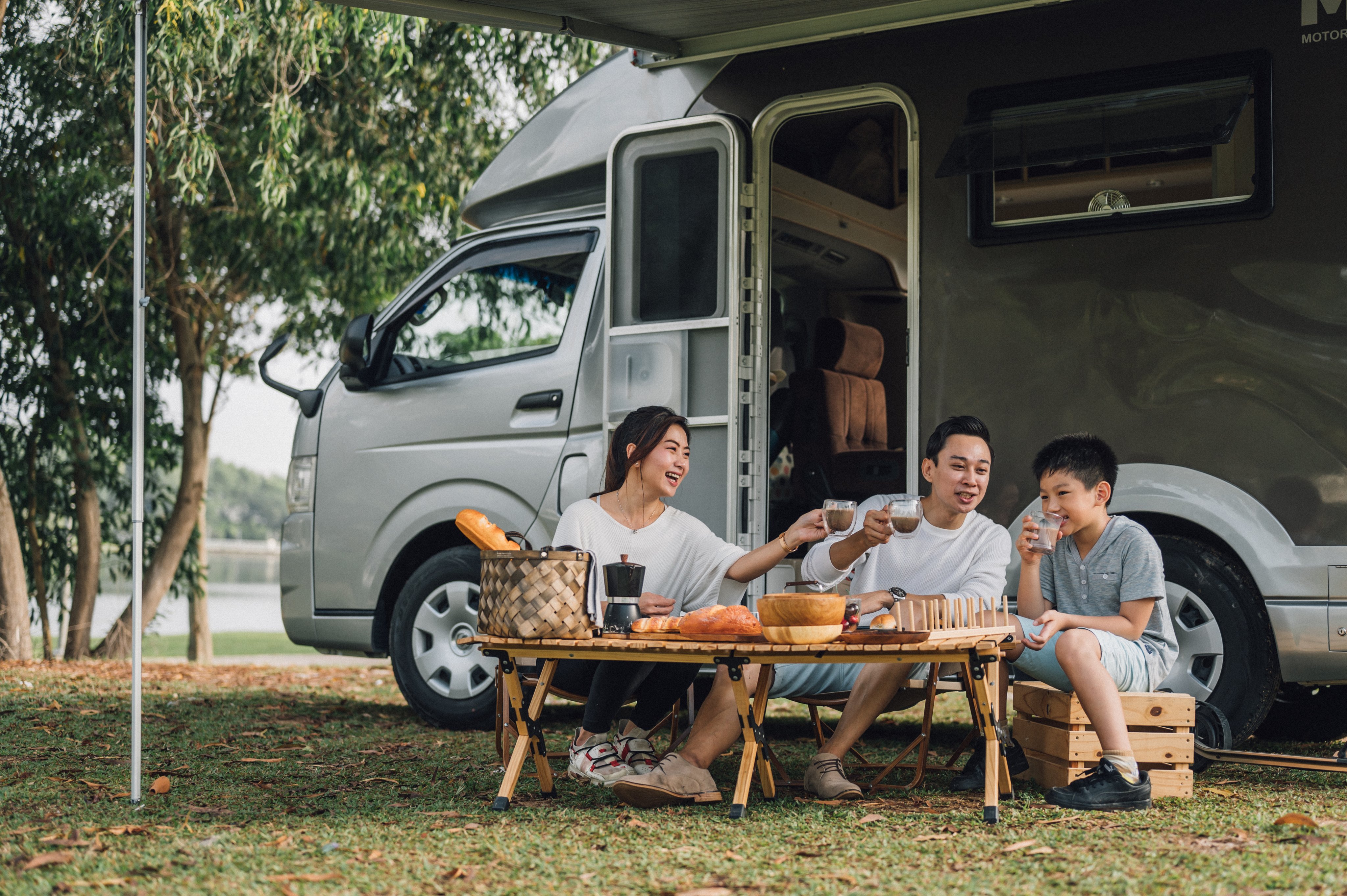 Happy Asian family talking at picnic table by the camper trailer in nature