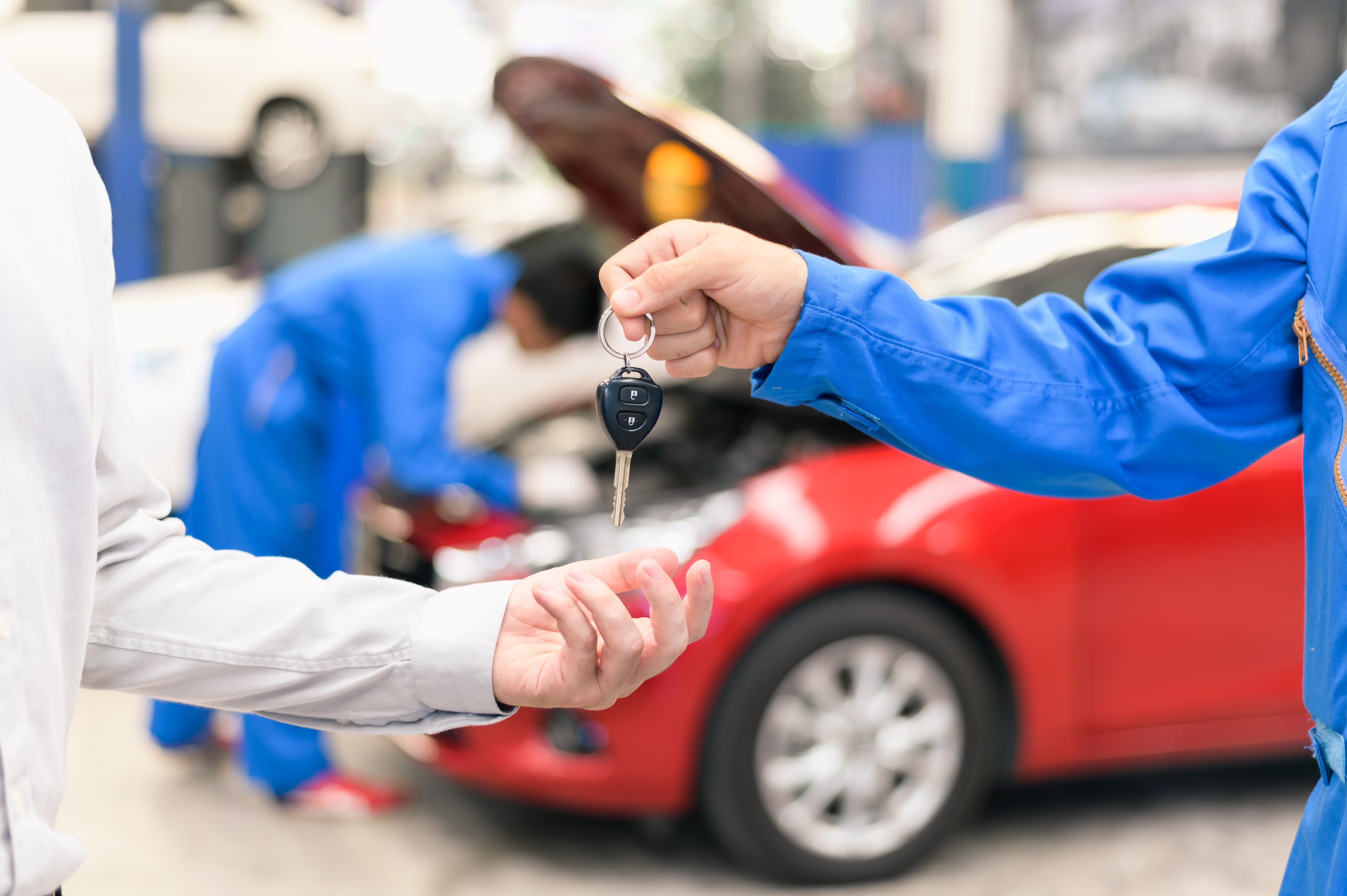 Vehicle owner customer receiving car key from car service technician after sending his car for repairing or check at automobile service center
