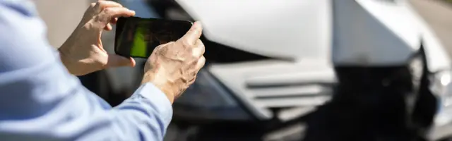Man inspecting and photographing his crashed car after a traffic accident