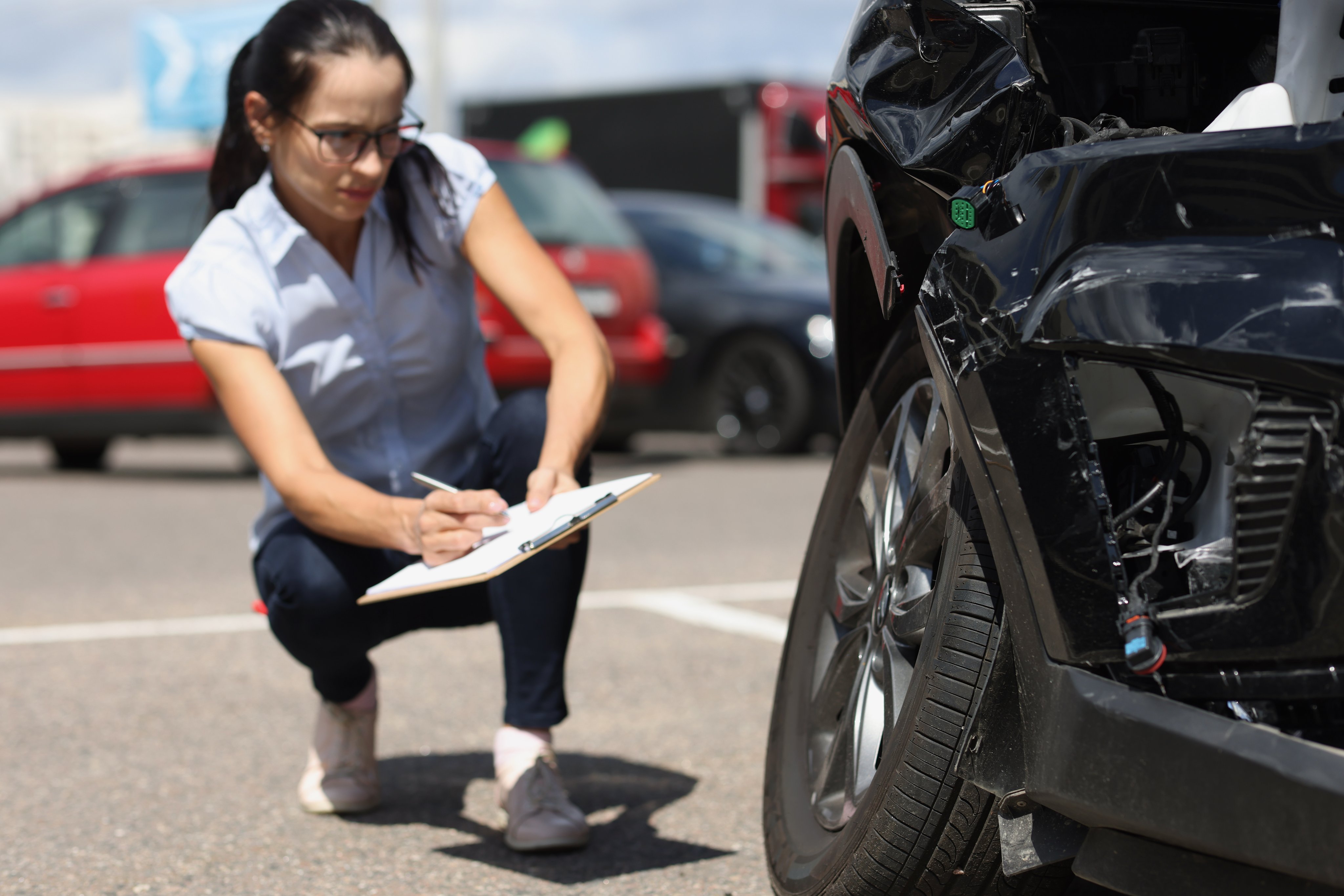 Woman inspector writing in documents on clipboard near broken car.