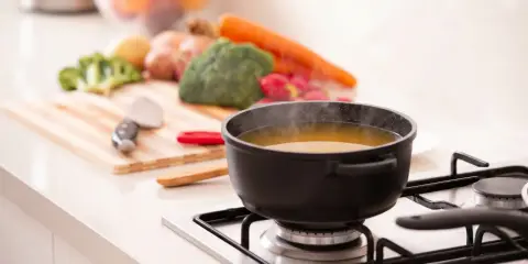Pot of soup simmering on a stovetop with fresh vegetables on a cutting board in the background