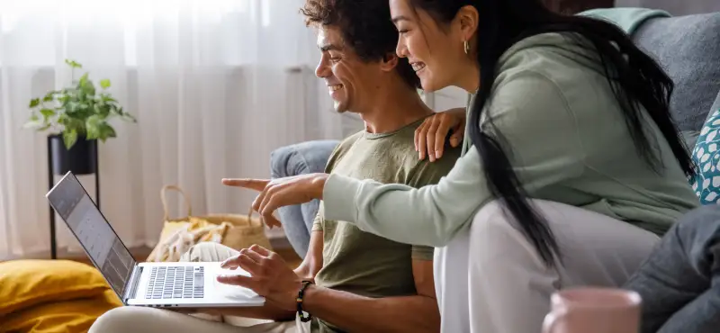 Young woman pointing at something on laptop screen while looking at online banking with her boyfriend