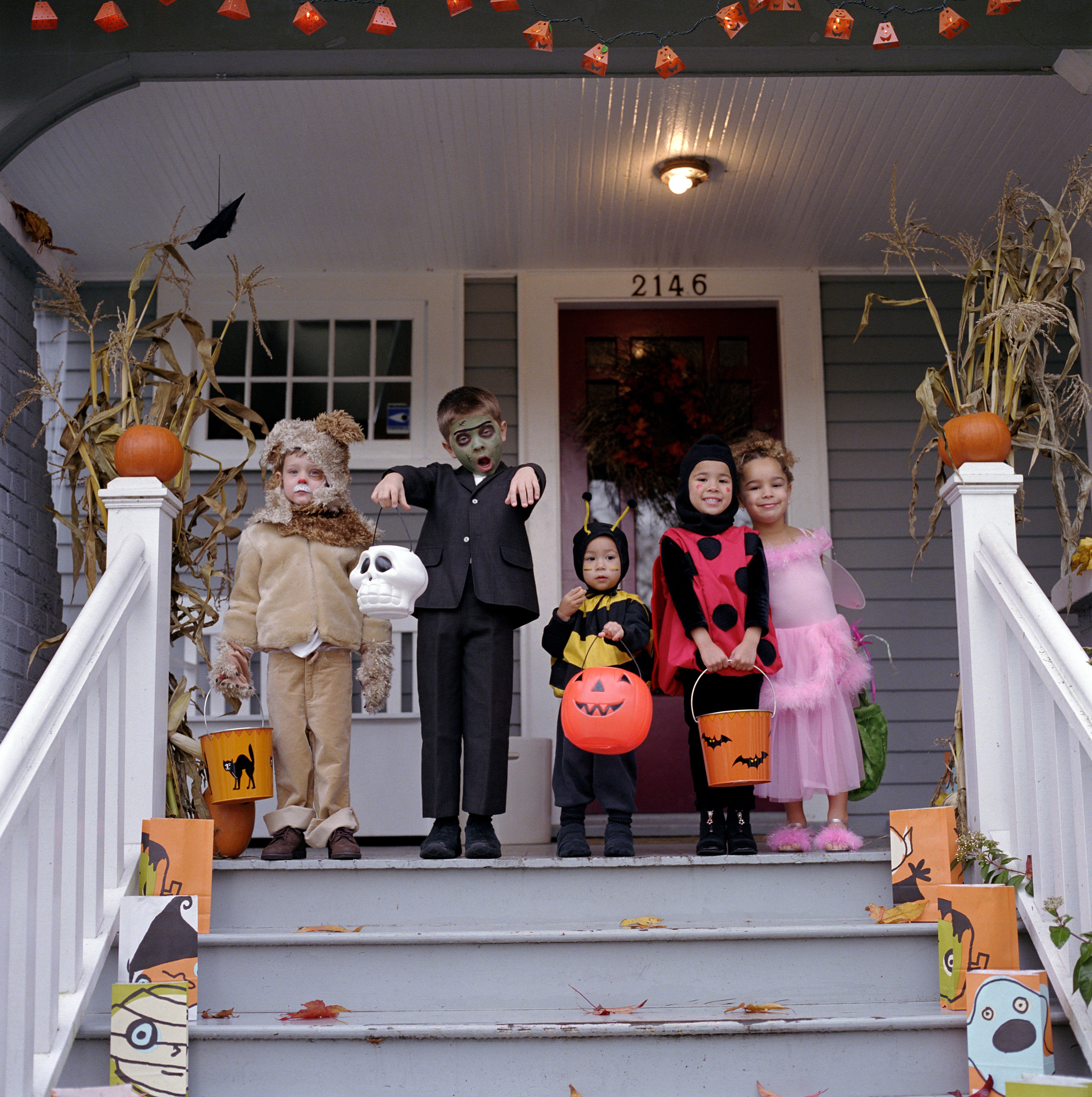 Five children wearing Halloween costumes, standing on a porch and making funny faces