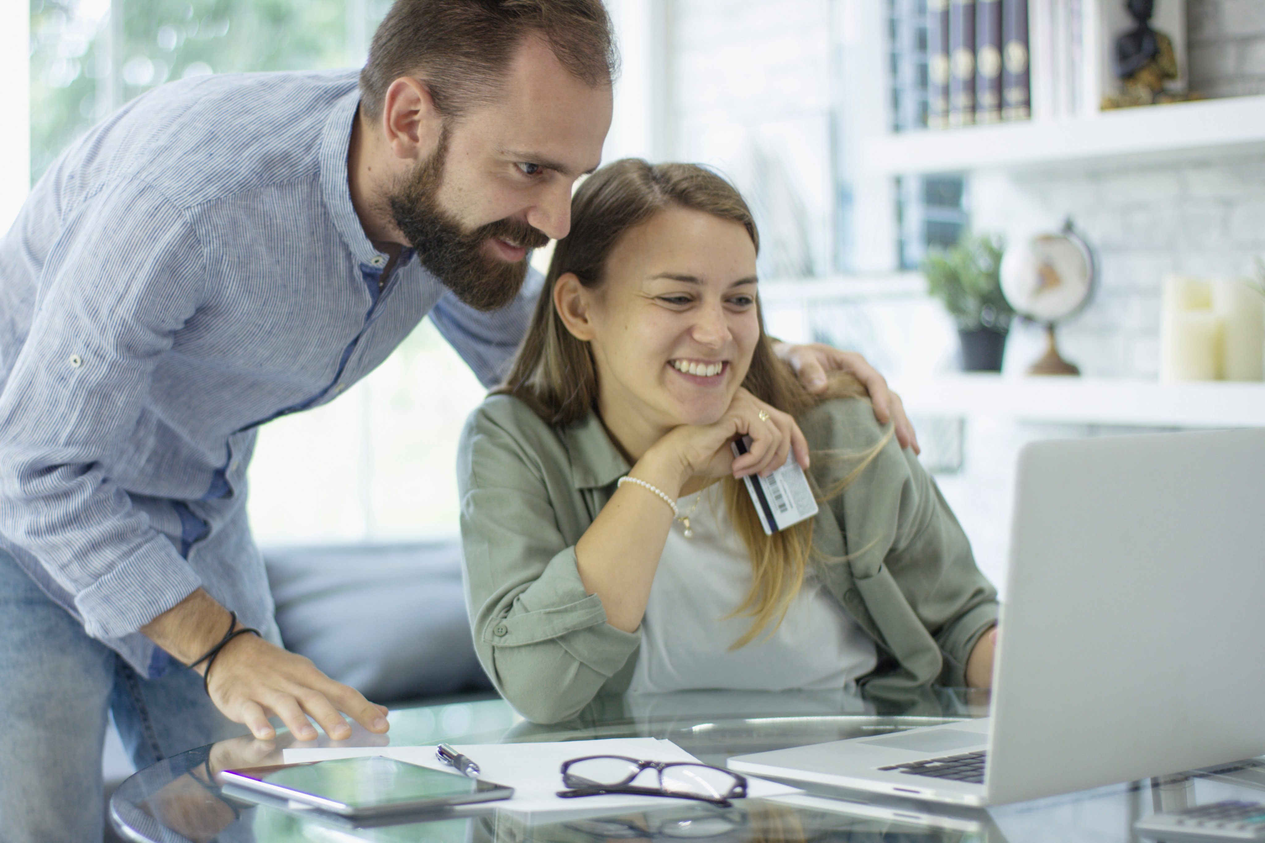 A husband and wife are indoors in a home office. They are wearing regular clothing while looking looking over their personal finances.